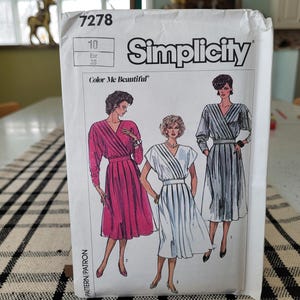 Puede incluir: Un sobre de patrón de costura Simplicity con ilustraciones de tres mujeres con vestidos. Los vestidos tienen corpiños cruzados y faldas plisadas. El sobre es blanco con el número 7278 y las palabras "Simplicity" y "Color Me Beautiful".