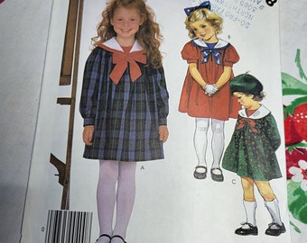 May include: A sewing pattern for children's dresses. The pattern includes three different styles: a plaid dress with a sailor collar, a red dress with a white collar, and a green dress with a white collar. The pattern is from McCall's and the pattern number is 2148.