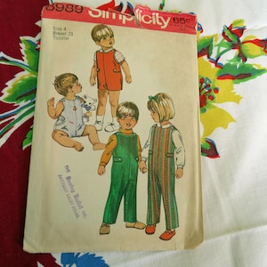 Puede incluir: Un sobre de patrón de costura vintage Simplicity, número 8989, para talla de niño pequeño 4 con un contorno de pecho de 58 cm. La portada presenta ilustraciones de niños con varios atuendos, incluidos petos, un pelele y un pichi, con el texto 8989 Simplicity 65c.