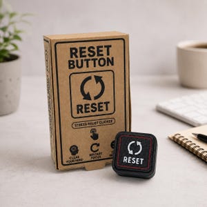 Puede incluir: Un clicker de alivio de estrés negro y cuadrado con un icono de flecha circular blanca y la palabra RESET impresa en la parte superior, colocado frente a su caja de cartón marrón con el texto RESET BUTTON, STRESS RELIEF CLICKER e iconos.
