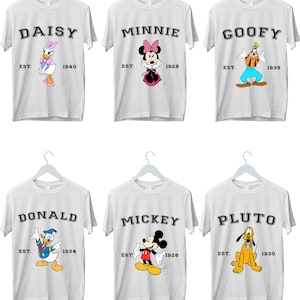 May include: Six white t-shirts featuring different Disney characters. The characters are Daisy Duck, Minnie Mouse, Goofy, Donald Duck, Mickey Mouse, and Pluto. Each shirt has the character's name printed at the top and "EST." and the year the character was created printed at the bottom.