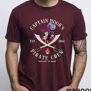 May include: Maroon t-shirt featuring Captain Hook's Pirate Crew design. The graphic includes Captain Hook, crossed swords, a skull, and the text "Look Alive, You Swabs!" and "EST. 1953".