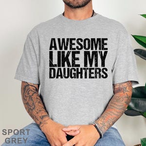 May include: Sport grey t-shirt with the text "AWESOME LIKE MY DAUGHTERS" in black. The shirt is a crew neck style and is made of a soft material. The shirt is a casual wear item.
