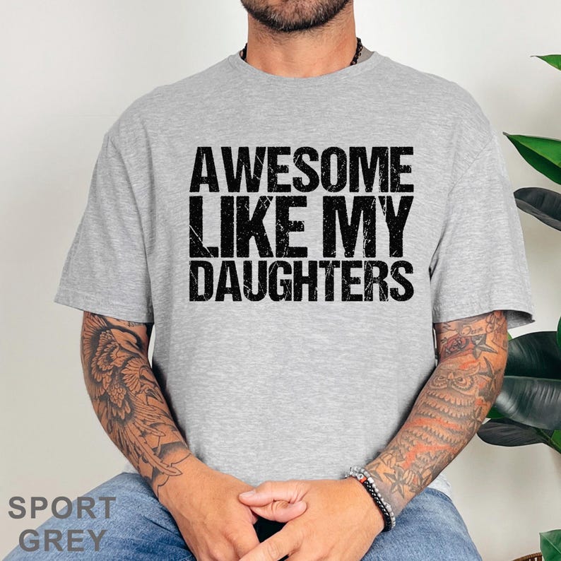 May include: Sport grey t-shirt with the text "AWESOME LIKE MY DAUGHTERS" in black. The shirt is a crew neck style and is made of a soft material. The shirt is a casual wear item.