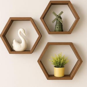 May include: Three hexagonal wooden shelves on a white wall. One shelf has a white swan ornament, another a green windmill, and the third a small yellow pot with a green plant. The shelves are a warm brown colour.