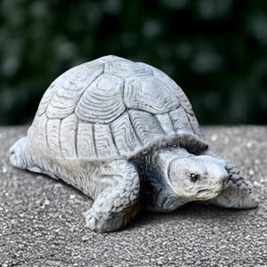 May include: A grey concrete turtle ornament with a textured shell and detailed features. The sculpture is in a realistic style, with visible legs, head, and a detailed shell pattern. Suitable for garden or home decor.