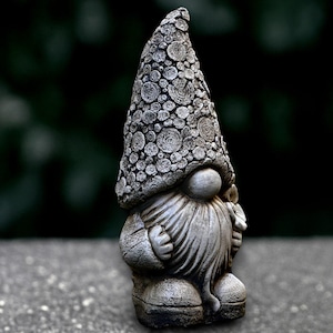 Puede incluir: Estatua de gnomo de jardín de piedra gris con un sombrero cónico texturizado y una larga barba. El gnomo está de pie, con las manos juntas. La estatua es de hormigón o material similar, apta para exteriores.