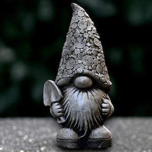 Puede incluir: Estatua de gnomo de jardín gris con barba larga y sombrero puntiagudo. El gnomo sostiene una pequeña pala y tiene un sombrero texturizado con un patrón circular. La estatua está hecha de un material similar a la piedra.