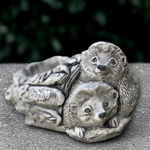May include: A gray stone hedgehog planter with two hedgehogs nestled together. The planter has a shallow bowl shape and is made of a textured stone material. The hedgehogs have detailed features, including small eyes and spiky backs.