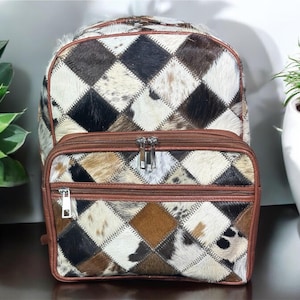 May include: A brown leather backpack with a patchwork design of different coloured cowhide. The backpack has two large compartments and a smaller front pocket.