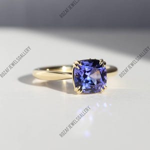 Op de afbeelding: Een gouden ring met een grote, vierkant geslepen, diepblauwe edelsteen. De band van de ring is glad en gepolijst, met de edelsteen op zijn plaats gehouden door delicate pootjes. De ring staat tegen een zachte, neutrale achtergrond.