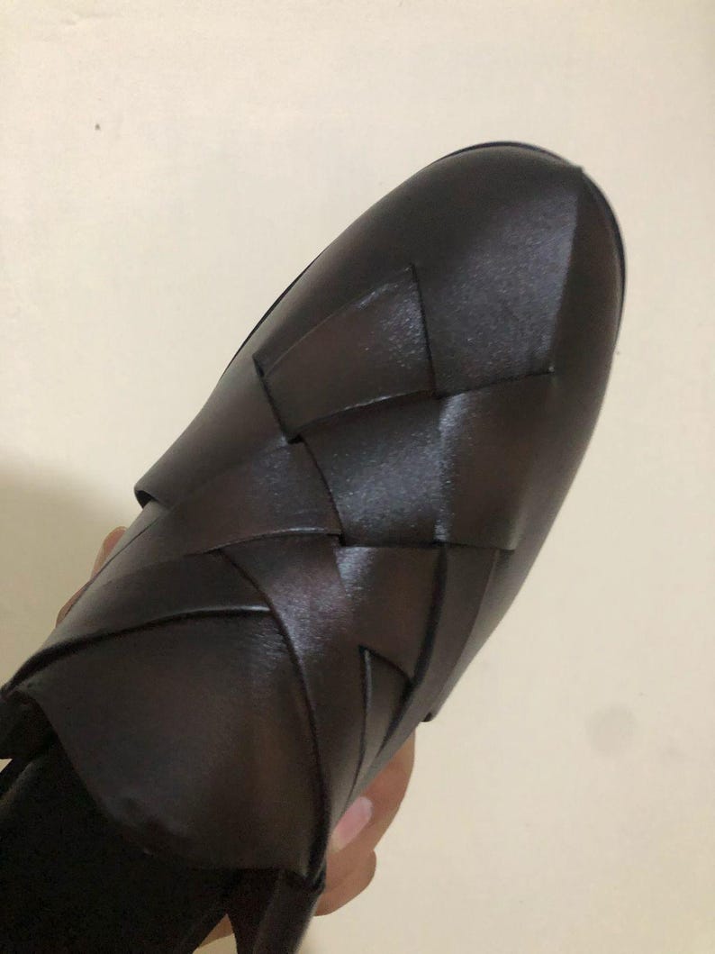May include: A dark brown slip-on shoe featuring a woven leather upper with wide, interlocking straps that create a textured, geometric pattern across the top. The shoe has a rounded toe and a smooth, polished finish on the leather surface.