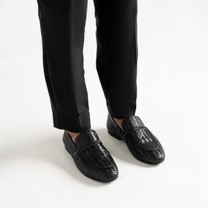 Premium black woven leather loafers for men worn with tailored trousers, showcasing luxury artisan craftsmanship, elegant braided penny loafer design, lightweight dress shoes, formal slip-on footwear, and timeless smart casual fashion styling.