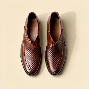 Pu&ograve; includere: Un paio di scarpe in pelle marrone con una trama intrecciata sulla tomaia e una finitura liscia sui lati. Le scarpe presentano una punta affusolata con una particolare costruzione a pannelli sovrapposti che crea una silhouette distintiva.