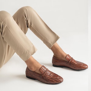 Men’s luxury woven leather loafers styled with beige trousers in modern smart casual outfit, featuring handcrafted braided leather design, elegant slip-on penny loafers, comfortable formal footwear, and sophisticated Italian-inspired men’s fashion shoes.
