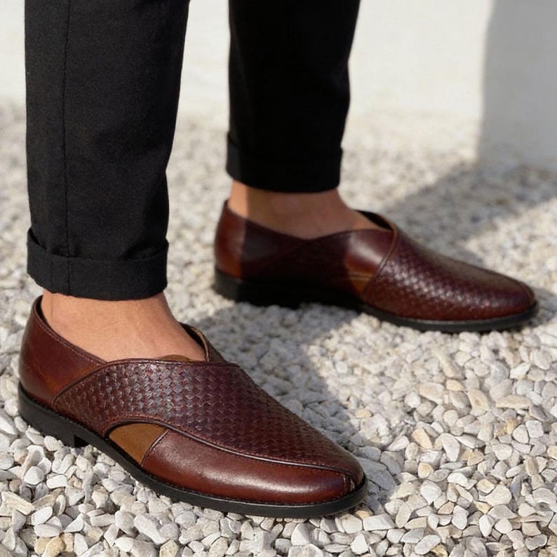 Pu&ograve; includere: Un paio di scarpe slip-on in pelle marrone scuro con una trama intrecciata sui pannelli superiori, una punta liscia in pelle e un tacco basso nero. Le scarpe presentano un caratteristico design asimmetrico ritagliato sui lati e una punta tonda.