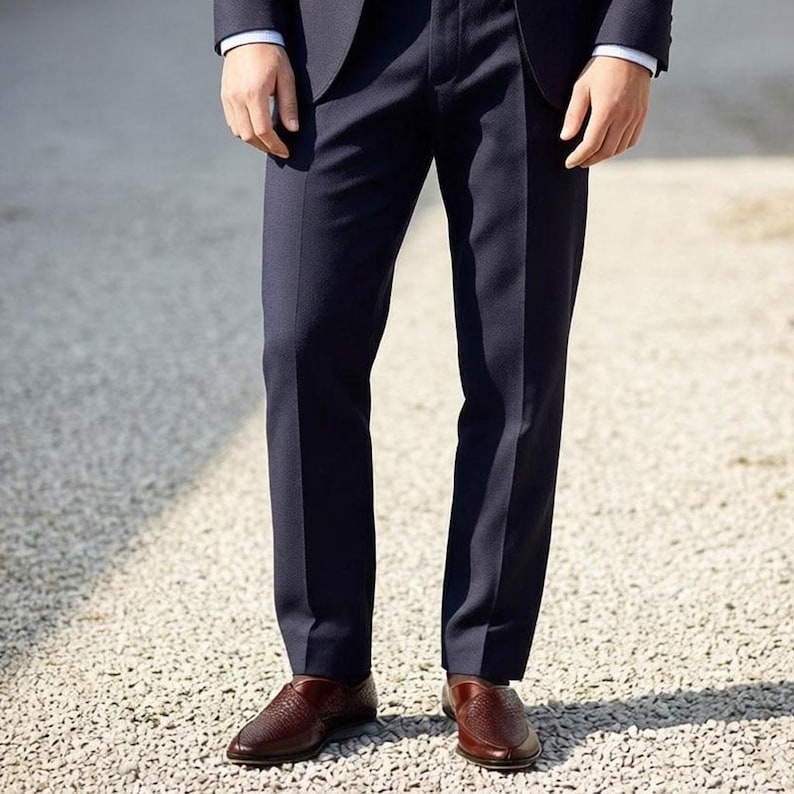 Pu&ograve; includere: Un paio di pantaloni eleganti blu navy scuro dal taglio dritto, abbinati a scarpe slip-on in pelle intrecciata marrone. I pantaloni presentano una piega stirata al centro di ogni gamba e le scarpe hanno una punta arrotondata.