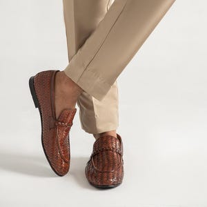 Premium brown woven leather loafers for men worn with tailored trousers, showcasing luxury artisan craftsmanship, elegant braided penny loafer design, lightweight dress shoes, formal slip-on footwear, and timeless smart casual fashion styling.