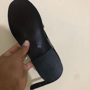 May include: A dark brown shoe sole with a smooth finish and a textured black heel piece. The number 10 is printed in white on the center of the sole. A thin, matching dark brown ankle strap with buckle holes extends from the side of the shoe.