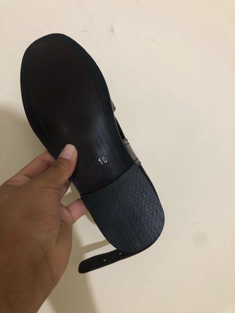 May include: A dark brown shoe sole with a smooth finish and a textured black heel piece. The number 10 is printed in white on the center of the sole. A thin, matching dark brown ankle strap with buckle holes extends from the side of the shoe.