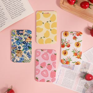 Può includere: Quattro custodie rettangolari per telefono con disegni di frutta. Una custodia presenta mirtilli e pancake, un'altra ha mango gialli, una terza fragole rosa e l'ultima pesche.