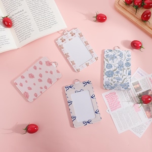 Może przedstawiać: Pięć uchwytów na identyfikatory z różnymi wzorami. Jeden ma różowe usta, drugi misie, trzeci niebieskie kokardy, a czwarty niebieskie wzory kwiatowe. Każdy ma przezroczyste okienko i srebrny pierścień.