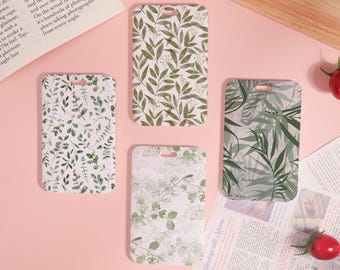 Puede incluir: Cuatro etiquetas rectangulares para equipaje con diseños botánicos. Las etiquetas presentan varios patrones de hojas verdes sobre un fondo blanco. Cada etiqueta tiene un pequeño agujero en la parte superior para sujetar. Las etiquetas están dispuestas sobre una superficie rosa.