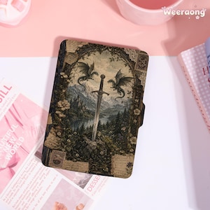 May include: A rectangular e-reader case featuring a detailed illustration of a sword embedded in a stone, flanked by two dragons, set against a backdrop of mountains, a lake, and a forest, all framed by ornate, vintage-style botanical patterns.
