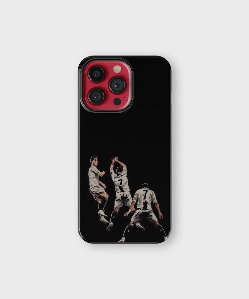 Puede incluir: Funda de tel&eacute;fono negra con una ilustraci&oacute;n estilizada de tres futbolistas en acci&oacute;n. Los jugadores visten uniformes blancos y negros. La funda tiene un borde negro y una lente de c&aacute;mara roja.