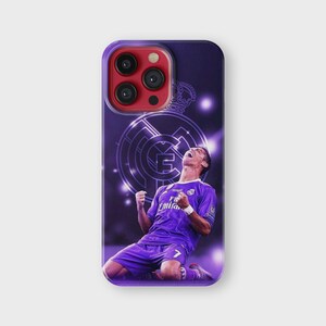 Puede incluir: Funda de tel&eacute;fono morada con un futbolista celebrando un gol. La funda tiene un fondo morado con el logo del Real Madrid y una corona. El jugador lleva una camiseta morada con el n&uacute;mero 7.
