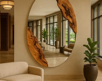 Puede incluir: Un espejo ovalado con marco de madera natural. El marco está hecho de dos piezas de madera con un patrón de vetas único. El espejo está montado en una pared beige en un espacio de vida moderno. La habitación incluye un sofá, una mesa de centro y plantas en macetas.