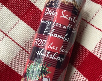 May include: A white stainless steel tumbler with a red and black plaid design. The tumbler features the text "Dear Santa, Sorry for all the F-bombs 2020 has been a shitshow" and a graphic of a red truck carrying a Christmas tree.