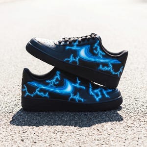 May include: Black sneakers with a blue lightning bolt design. The shoes have a black sole and laces, with a blue swoosh and lightning bolt graphics on the sides. The sneakers are stacked on top of each other.
