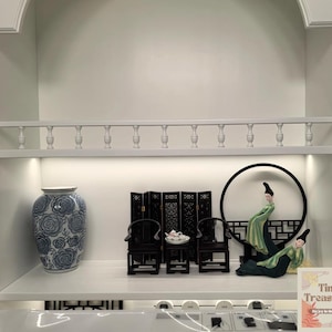 May include: A white shelf with a blue and white porcelain vase, a black screen, two black chairs, a tea set, a round black frame with two figurines in green and white robes, and a card that says "Tiny Treasures" with the text "Say yes to tiny treasures".