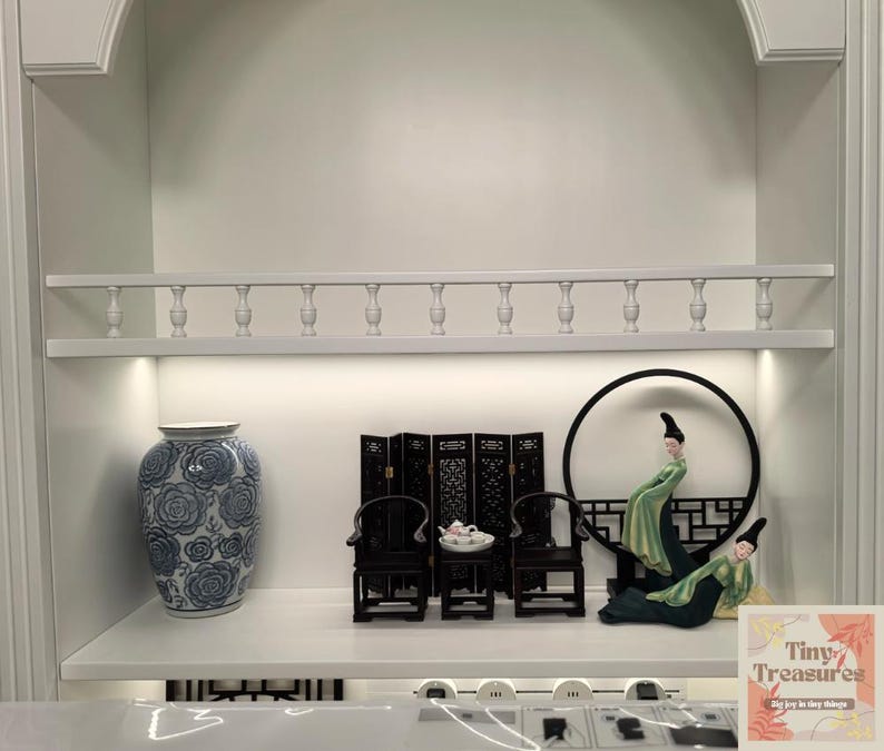 May include: A white shelf with a blue and white porcelain vase, a black screen, two black chairs, a tea set, a round black frame with two figurines in green and white robes, and a card that says "Tiny Treasures" with the text "Say yes to tiny treasures".