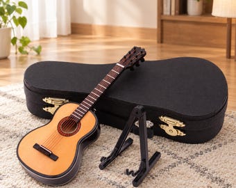 May include: A miniature acoustic guitar with a light wood-toned body and dark fretboard, accompanied by a black folding display stand and a black hardshell carrying case featuring gold-colored metal latches and hinges for secure storage.