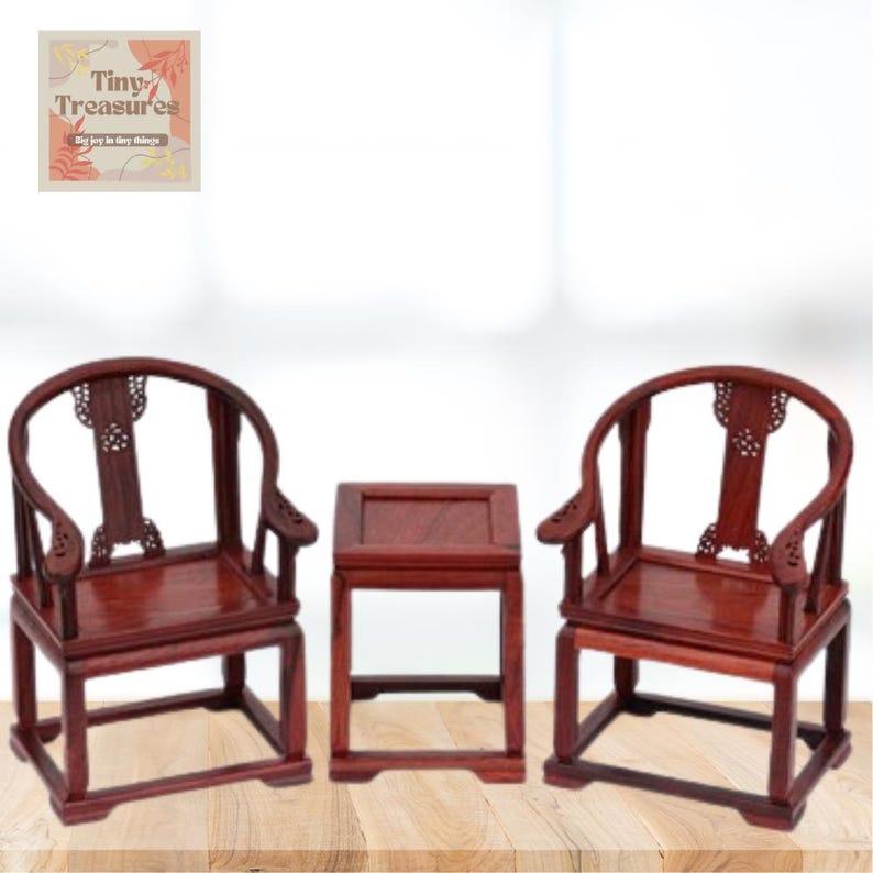 May include: A set of three miniature wooden furniture pieces, including two chairs and a table. The chairs have a curved back and intricate carvings. The table is square and has a simple design. The furniture is made of a dark reddish-brown wood.