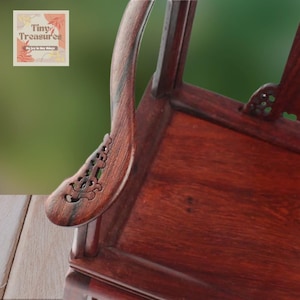 May include: A close-up of a dark red wooden chair with intricate carvings on the armrest. The chair is made of solid wood and has a traditional design.