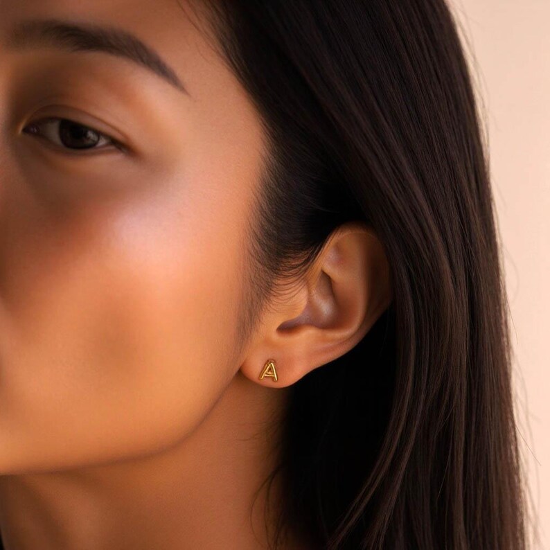 K&ouml;nnte beinhalten: Nahaufnahme eines Ohrs mit einem goldenen Ohrring in Form des Buchstabens 'A'.