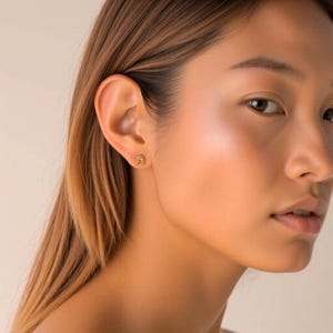 K&ouml;nnte beinhalten: Nahaufnahme eines Ohrs mit einem goldenen Initial 'A' Ohrstecker.