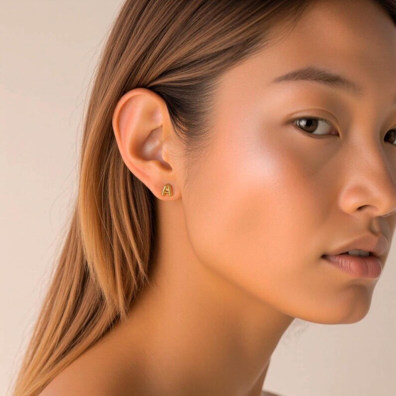 K&ouml;nnte beinhalten: Nahaufnahme eines Ohrs mit einem goldenen Initial 'A' Ohrstecker.