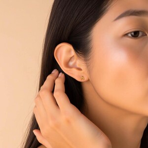 K&ouml;nnte beinhalten: Nahaufnahme eines Ohrs mit einem goldenen Ohrring in Form des Buchstabens 'A'.