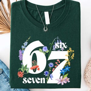 a green t-shirt with the number "67" printed on it, surrounded by various clothing items and accessories, including jeans, a pair of sneakers, and a sweater.
