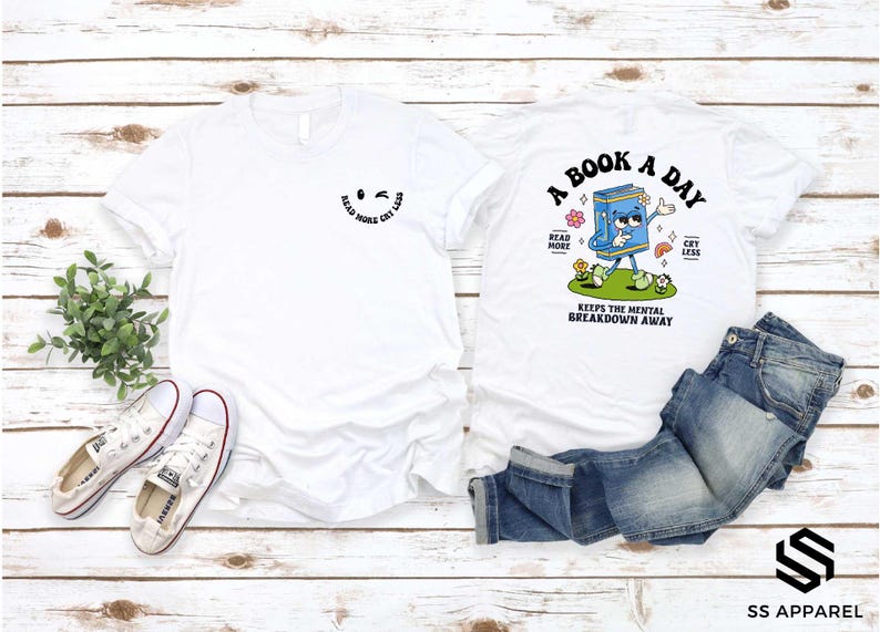 a white t-shirt with a graphic design and text, a pair of jeans, and some sneakers, all laid out on a wooden surface.