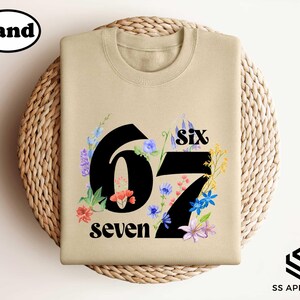 A beige t-shirt with a floral design and the number "67" printed on it, placed on a woven basket.
