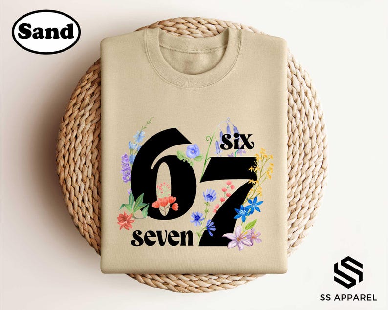 A beige t-shirt with a floral design and the number "67" printed on it, placed on a woven basket.