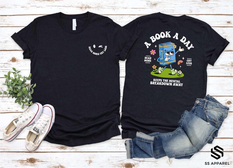 a black t-shirt with a graphic design and text, along with a pair of jeans and sneakers, all laid out on a wooden surface.