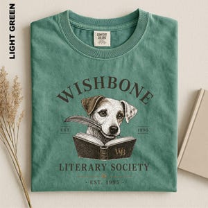 A green t-shirt with a graphic design featuring a dog holding a book, along with text that reads "Wishbone Literary Society" and "Est. 1995".