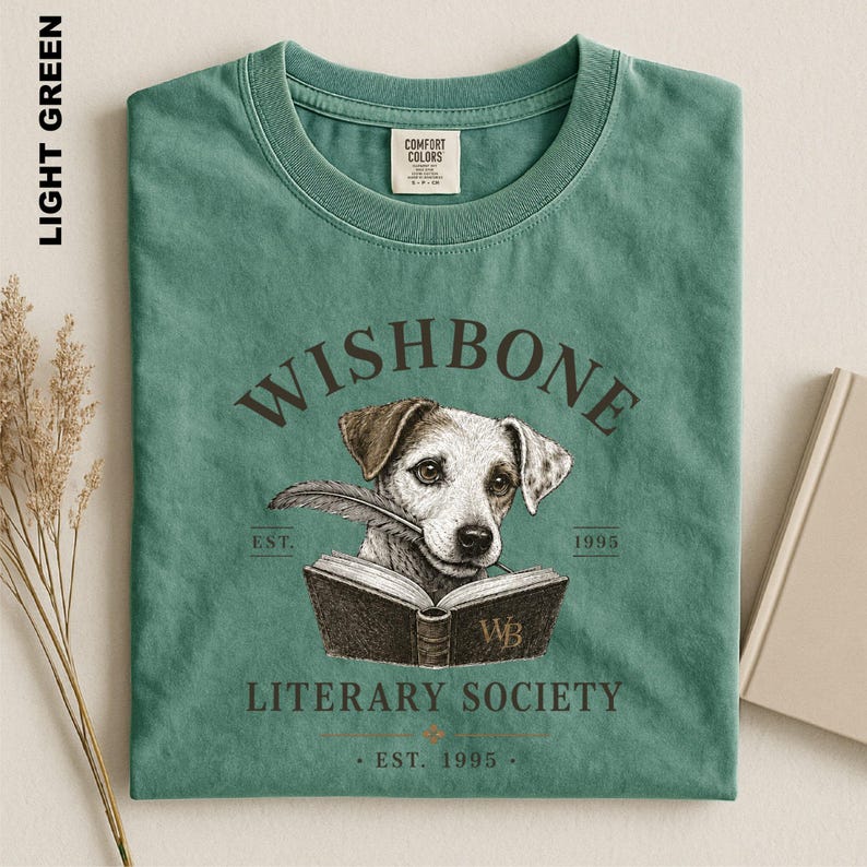 A green t-shirt with a graphic design featuring a dog holding a book, along with text that reads "Wishbone Literary Society" and "Est. 1995".