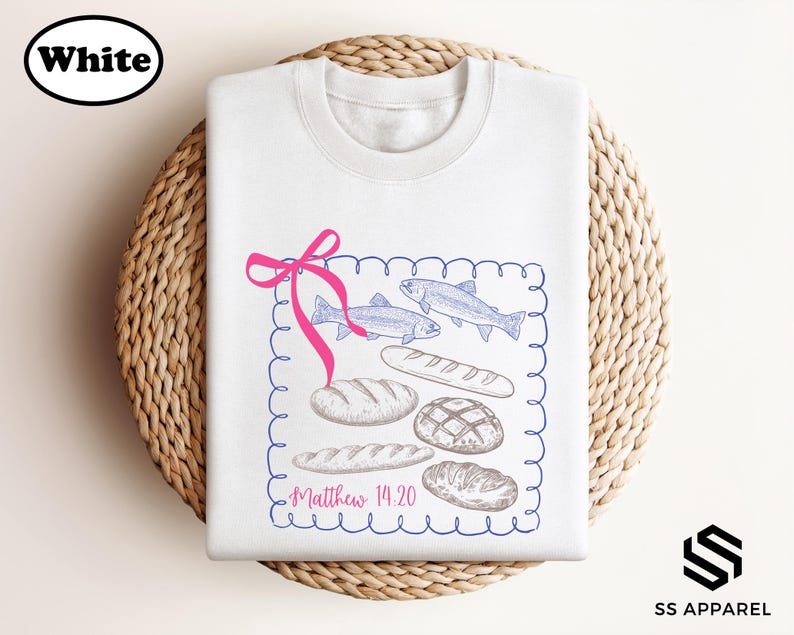 A white t-shirt with a graphic design featuring illustrations of bread and fish, along with the text "Matthew 14:20" printed on it.